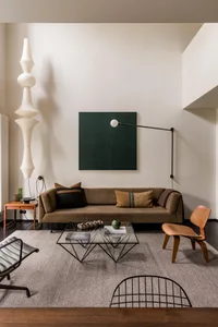 A modern living room featuring a brown fabric sofa, glass coffee table, and wood accent chair.