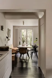 Modern dining room with transparent vase on wooden table, black chairs, and glass windows showcasing trees.
