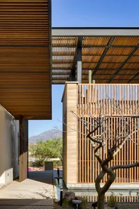 A modern architectural structure featuring a wooden pergola, concrete base, and metal beams.