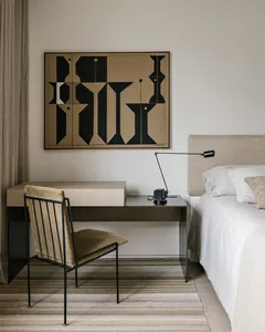 A minimalist bedroom with a wooden desk, metal chair, and fabric bedding.