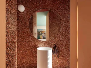A modern bathroom features walls with a speckled granite texture and a cylindrical white pedestal sink.