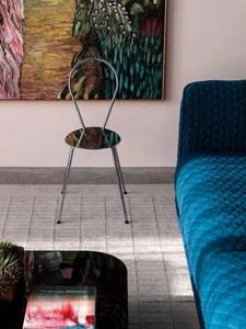 A modern interior with a metallic frame chair, blue quilted sofa, and abstract paintings.