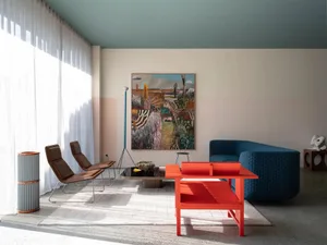 A modern living room featuring colorful furniture, a blue upholstered armchair, and a bright red coffee table. There's also a
