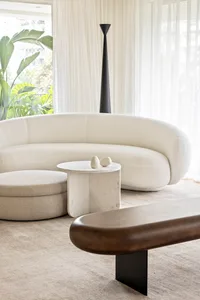 A modern living room featuring a sleek white sofa, a wooden bench, and a marble coffee table with a high black-standing lamp 