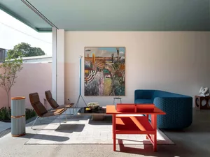 A modern living room featuring metal chairs, a fabric sofa, and wooden coffee table and side tables with plants and artwork.