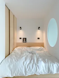 A minimalist bedroom with white walls, a wooden bed frame, and white towels.