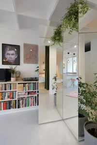 A modern white living space featuring glass walls, a green plant, and a white floor, with a white bookshelf filled with books
