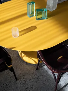 A close-up view of a round, yellow metal dining table with modern, geometric glass candle holders.