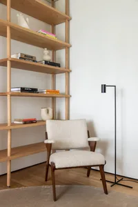 A mid-century study space featuring a wooden shelf with books and decorative items, a white upholstered chair, and a modern b