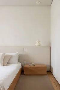 Modern minimalist bedroom featuring a wooden bed with a fabric headboard, pendant light, and minimalistic decor.