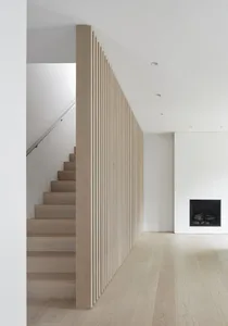 A minimalist living room with wooden stairs, white walls, and a wall-mounted fireplace.