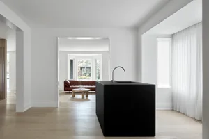 Modern interior design featuring a black kitchen island with a white countertop, contrasting light-colored wood floors, and a
