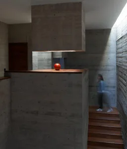 A minimalist interior design featuring concrete walls and a wooden counter with a red apple.