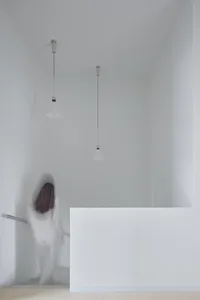 A minimalist white interior space with a person climbing stairs.