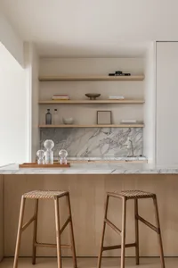 A modern kitchen with white marble countertops and wooden stools.