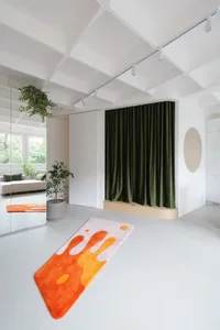 A modern living room with a white plaster floor, green curtains, and an orange and white rug.