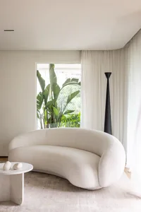 Modern living room featuring a curved white sofa, white curtains, and a tall black lamp.