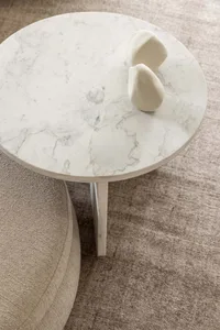 A modern coffee table with a round white marble top adorned with a minimalist white sculpture.