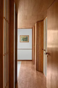 A minimalistic corridor with wooden walls, windows, and floors, featuring a framed artwork on the wall.