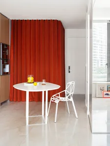 A minimalist kitchen featuring a white metal table and chair with a red curtain and white door in the background.