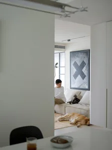 A minimalist living room with a white couch, concrete ceiling, and a person sitting on the couch with a cat and a sleeping do
