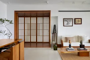 A minimalist living room with white walls and wooden furniture, featuring a white sofa, coffee table, and decorative elements