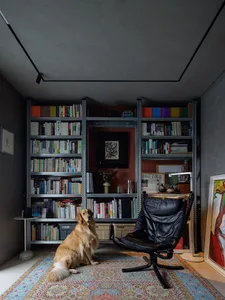 A living room with an industrial design featuring metal shelves filled with books, a wooden armchair, and a carpeted floor.