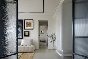 A minimalist living room with a textured glass wall, a cozy sofa, and framed artworks hanging on the wall.