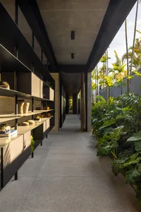 A modern hallway with concrete flooring and walls, featuring built-in shelves and greenery lining the walls.