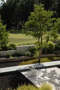 Modern residential patio featuring a concrete patio, stone planters, and gravel landscaping, surrounded by a forested backdro