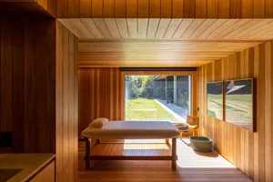 A modern spa room featuring a wooden treatment bed and natural light from a large window.