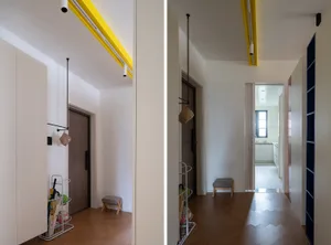 A minimalist interior with hardwood floors, showing a corridor with yellow lighting and a view into a kitchen area.