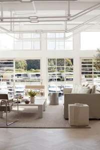 A modern, minimalist living room with neutral tones, featuring a sofa, coffee table, and large windows overlooking the marina