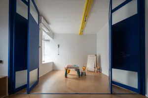 A modern children's playroom with blue double doors and wooden flooring, featuring a play table and easel.