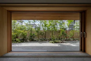 A modern garden with hardwood flooring and plants, viewed from a wooden doorway.