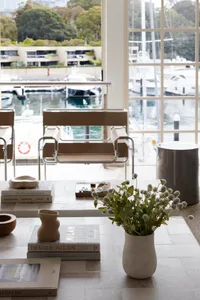 A modern living room featuring wooden furniture, books, and a vase of flowers with white blooms on a table by a large window 