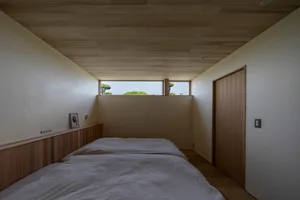 A modern residential bedroom with wood elements, including a bed with white linens and a wooden headboard, featuring a small 