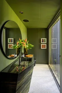 A modern bathroom with green stone countertops and mirror, featuring a vase of flowers and a window.