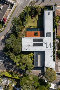 An aerial view of a modern residential home with concrete exterior walls and a wooden rooftop deck surrounded by lush greener