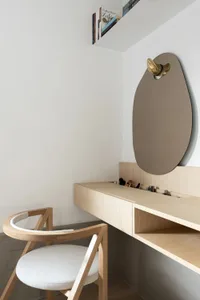 Modern, minimalist wooden desk and chair setup with a round mirror and books on the wall.