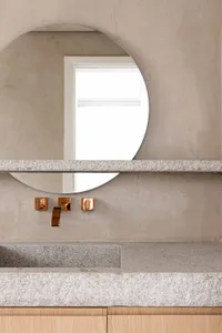 Modern minimalist bathroom featuring a concrete countertop and sink with a round mirror and brass fixtures.