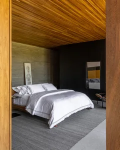 A minimalist bedroom with a white bed, grey carpet, and wooden ceiling.