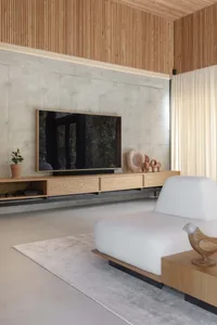 A modern, minimalist living room with concrete walls and a wooden TV stand and furniture.