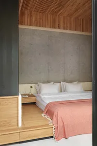 A minimalist bedroom featuring a wooden bed frame with a concrete wall and wooden ceiling.