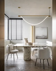 A modern dining room featuring a marble table and minimalist chairs, illuminated by a contemporary light fixture.