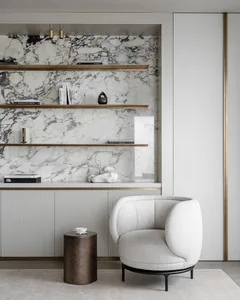A modern living room with white marble walls and a white upholstered chair.