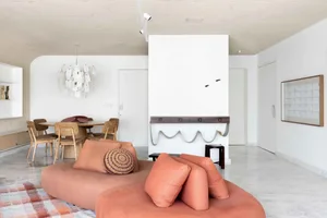 A minimalist living space featuring white walls and stone flooring with a comfortable sofa, dining area, and functional zones