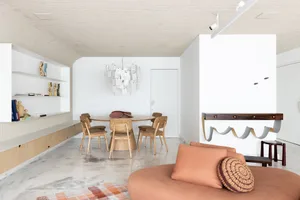 A minimalist residential interior with a round dining table surrounded by chairs, a mauve-colored sofa with a woven circular