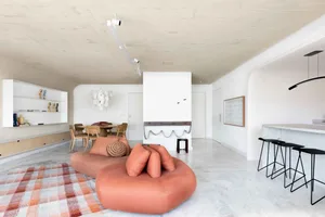 A modern living space featuring a comfortable lounger, high stools, and a sleek bar counter.