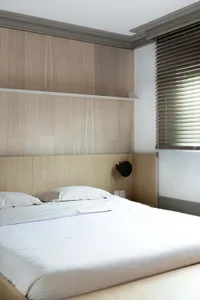 A modern minimalist bedroom with a wooden headboard and light-colored bedding.
